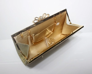 Close-up of golden glitter evening clutch featuring a rhinestone bow clasp and satin lining