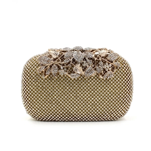 Detailed macro view of the rhinestone-studded leaf buckle on the gold evening clutch bag
