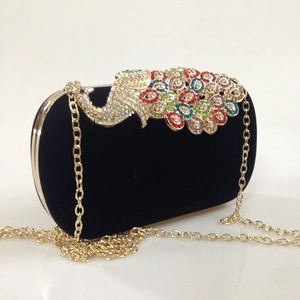 Detail of velvet clutch bag with a colorful crystal peacock clasp and gold chain