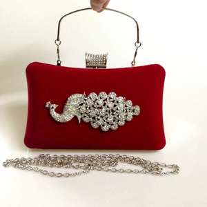 Close-up of a red velvet evening clutch with a sparkling rhinestone peacock design