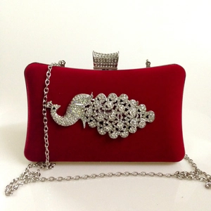 Detail of red velvet evening clutch featuring a sparkling rhinestone peacock ornament and chain