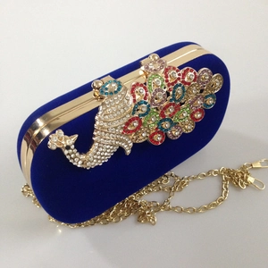 Macro detail of royal blue velvet clutch featuring a colorful rhinestone peacock ornament