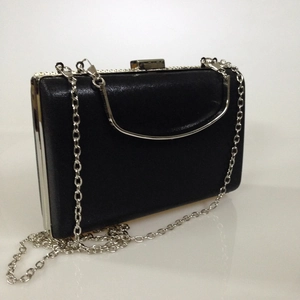 Detail of a black evening clutch bag with silver metal frame and detachable chain strap
