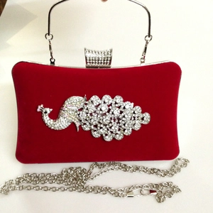 Macro view of red velvet evening bag featuring crystal peacock and metal handle detail