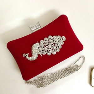 Detail of red velvet evening clutch featuring a sparkling rhinestone peacock and silver chain