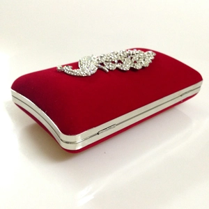 Detail showing red velvet texture and sparkling peacock rhinestone ornament on evening bag