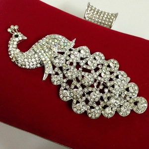 Close-up of red velvet evening bag featuring a sparkling crystal peacock embellishment