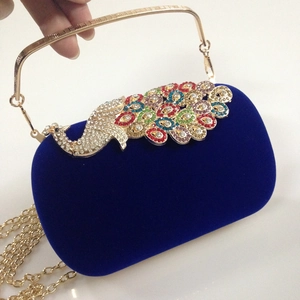 Close-up of blue velvet evening bag featuring crystal peacock clasp and gold metal handle