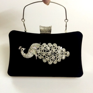 Close-up of black velvet evening bag featuring crystal peacock decor and metal handle