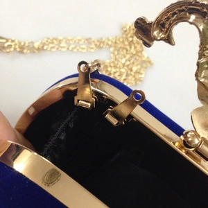 Detail of blue velvet evening bag with gold bird clasp and chain strap close-up