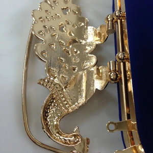Detail of golden floral hollow frame and crown clasp on royal blue velvet evening bag