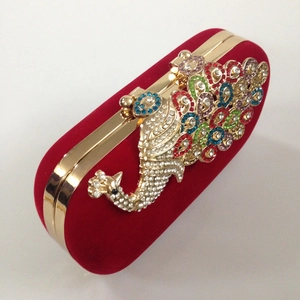 Detailed close-up of a golden peacock clasp with multi-colored rhinestones on a red velvet bag