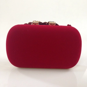 Close-up of deep red velvet clutch bag featuring gold metal clasp and sparkling jewels