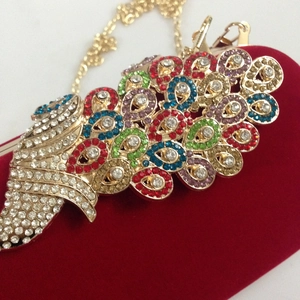 Detail of red velvet evening clutch featuring colorful peacock crystal embellishments