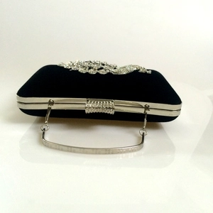 Detail of black velvet evening clutch featuring silver rhinestone floral decor and metal handle