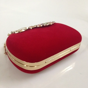 Detail of red velvet evening clutch with gold metal frame and sparkling crystal peacock clasp