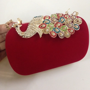 Macro detail of red velvet clutch bag featuring a gold peacock crystal-encrusted design