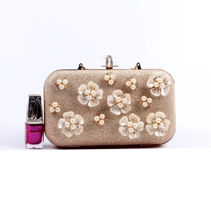 Macro shot of 3D white flower accents and pearls on a gold glitter evening clutch bag