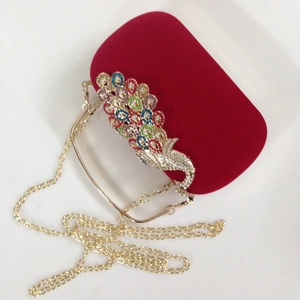 Detailed close-up of a red velvet evening clutch with a colorful rhinestone peacock ornament