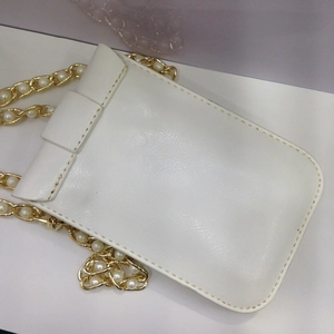 Detail einer weißen Mini-Tasche aus Kunstleder mit Goldkette und eleganten Perlen
