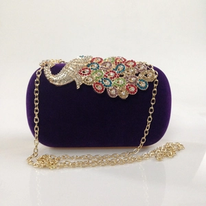 Close-up of velvet evening bag with colorful rhinestone peacock clasp and gold chain