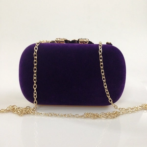 Detail of dark purple velvet clutch bag with golden jewel clasp and metal chain strap