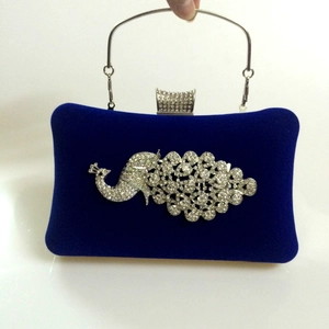 Detail of navy velvet evening clutch featuring a sparkling rhinestone peacock and metal handle