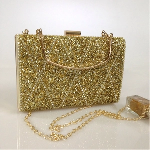 Detail of gold evening clutch bag with sequins, metal handle, and fine chain strap