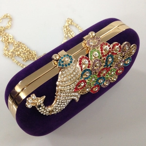 Close-up of a purple velvet evening clutch with a colorful peacock rhinestone ornament