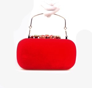 Close-up of red velvet evening clutch with golden handle and crystal floral clasp