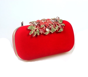 Macro detail of red velvet clutch with luxury floral metal clasp and colorful rhinestones