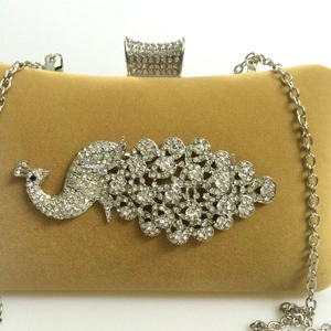 Detail of golden velvet evening bag featuring a crystal peacock and silver chain