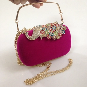 Close-up of fuchsia velvet evening bag with colorful rhinestone peacock and gold handle