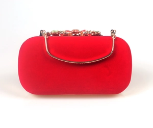 Close-up of red velvet evening clutch with gold handle and colorful rhinestone floral clasp
