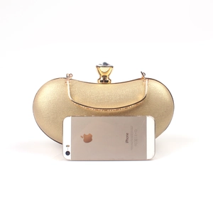 Detailed texture of golden evening clutch with oversized gemstone clasp and snake chain handle