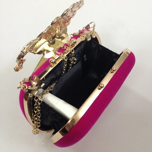Macro view of fuchsia velvet clutch bag with golden butterfly diamond lock and gold chain
