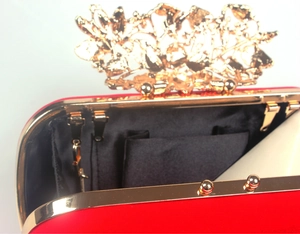 Detail view of red velvet evening clutch with golden floral clasp and black lining