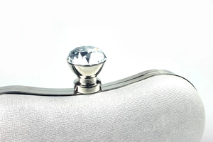 Close-up of elegant white fabric clutch with sparkling diamond clasp and metal frame