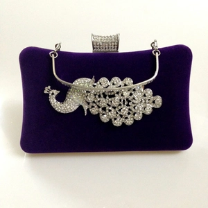 Close-up of a purple velvet evening bag featuring a crystal peacock design and silver handle