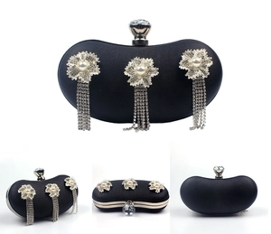 Detail of black evening clutch featuring crystal flowers, long tassels, and gemstone clasp
