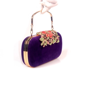 Detail of purple velvet evening bag featuring crystal leaf clasp and gold handle