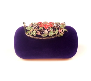 Detailed close-up of velvet evening bag with ornate floral crystal clasp and gold metal trim