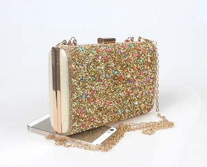 Close-up of golden evening clutch with colorful rhinestones and detachable chain strap