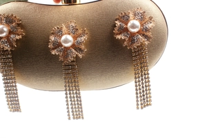 Detail of luxury gold clutch featuring metallic flowers, pearl centers and rhinestone tassels