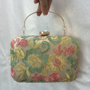 Macro detail of floral embroidery and gold ring handle on a champagne evening clutch bag