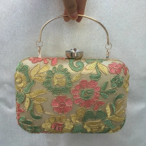 Detail of floral embroidery evening bag with golden metal handle and crystal clasp