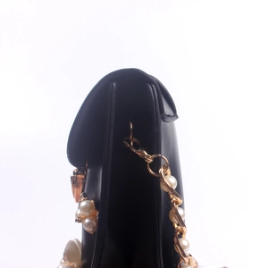 Detail der schwarzen Lederhandtasche mit goldener Kette und weißen Perlen-Akzenten