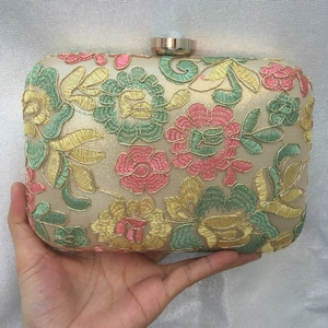 Close-up of floral embroidery detail and gold metal clasp on a vintage evening clutch bag