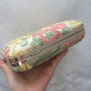 Detailed embroidery of pink and yellow flowers on an elegant ivory evening handbag