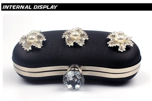 Detail of black clutch bag with silver metal flowers, pearls, and a large crystal clasp